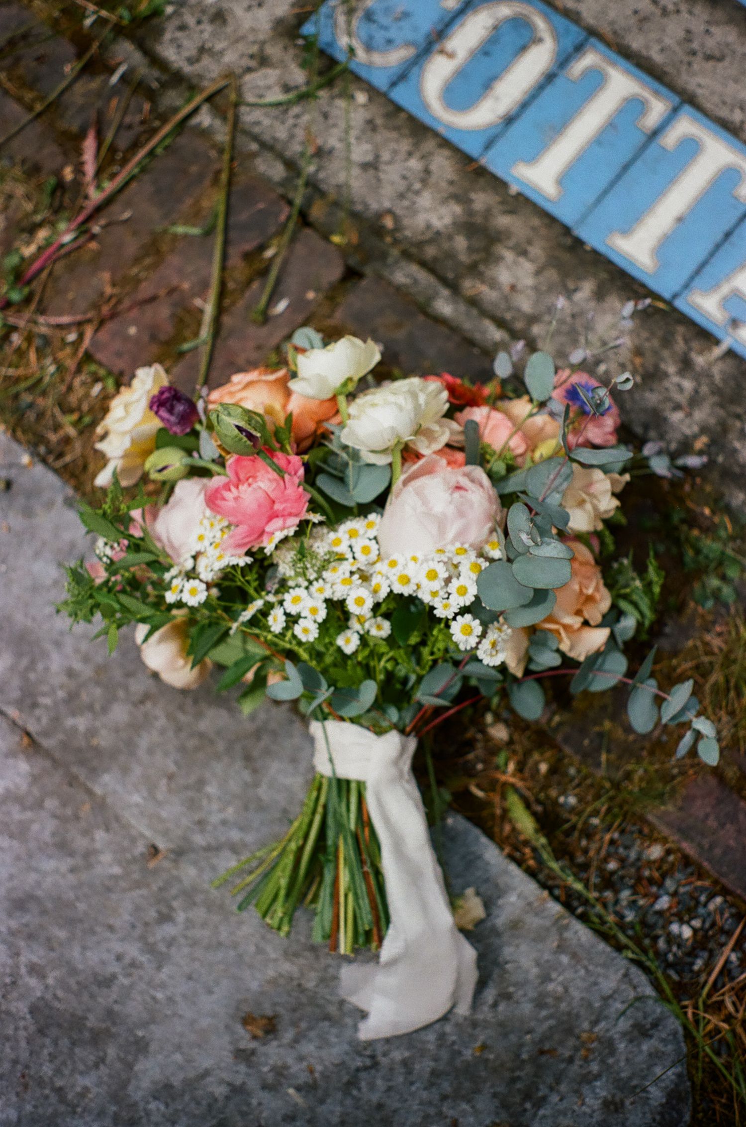 Beautiful bridal bouquet with pink and white roses, eucalyptus leaves, and delicate daisies arranged against textured stone surface.