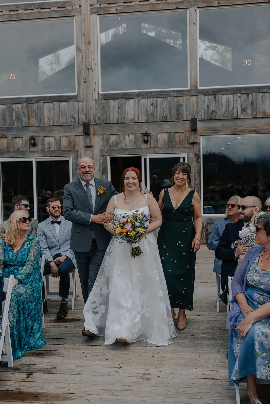 Wedding party gathered on rustic wooden deck with mountain backdrop.