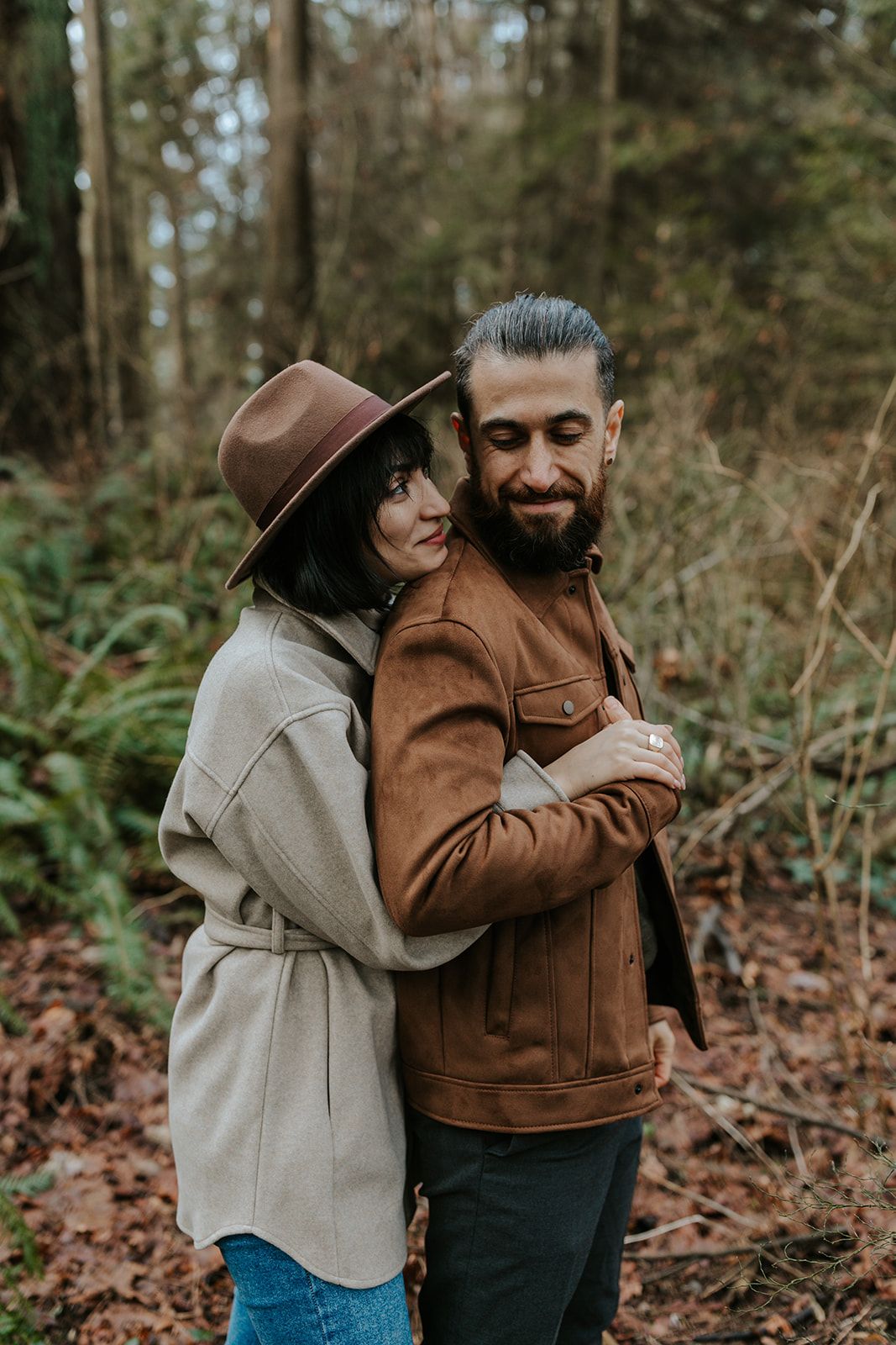 A couple in casual outerwear shares playful moments in an autumn forest setting.