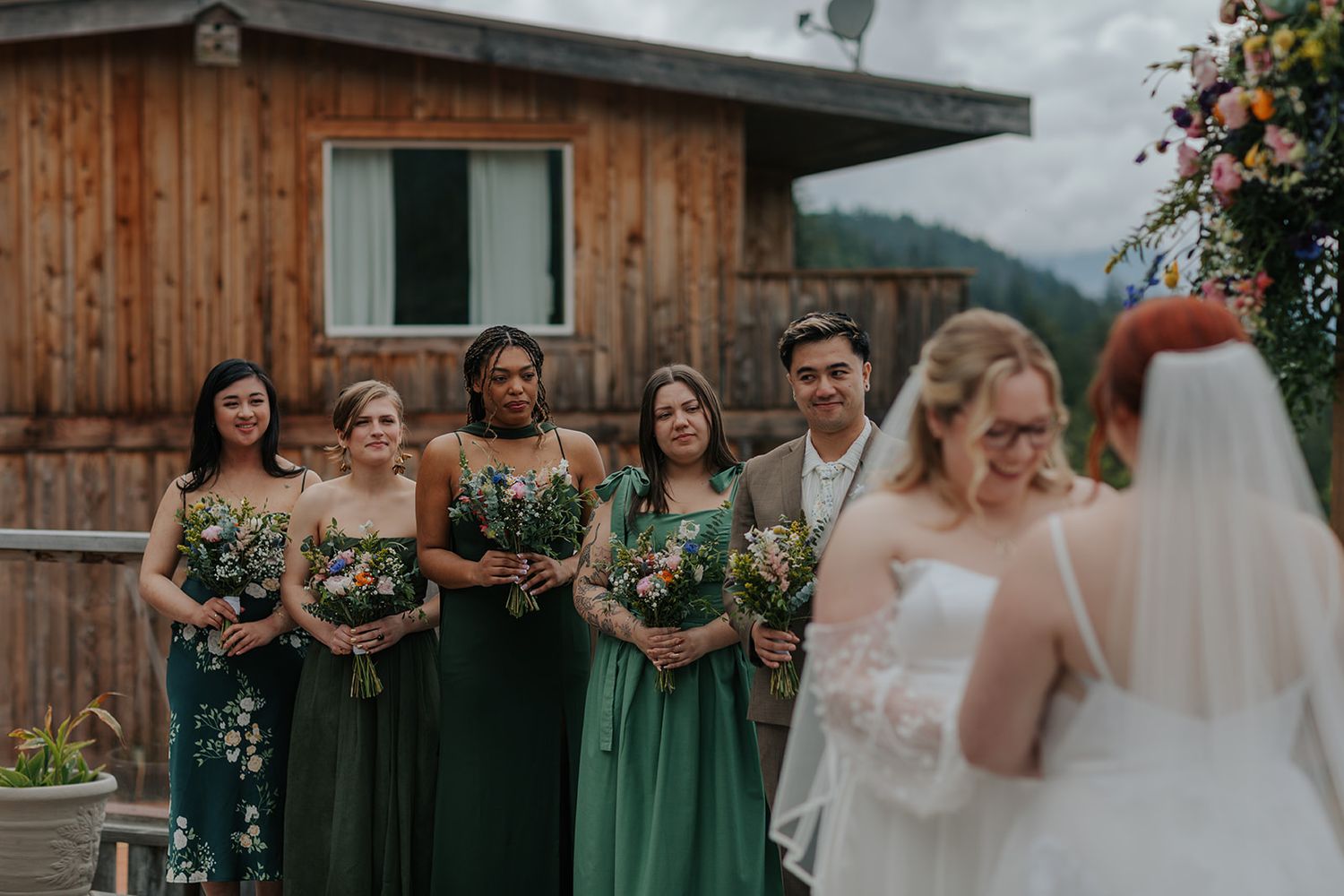 Wedding party members wearing green dresses standing outside a wooden building.