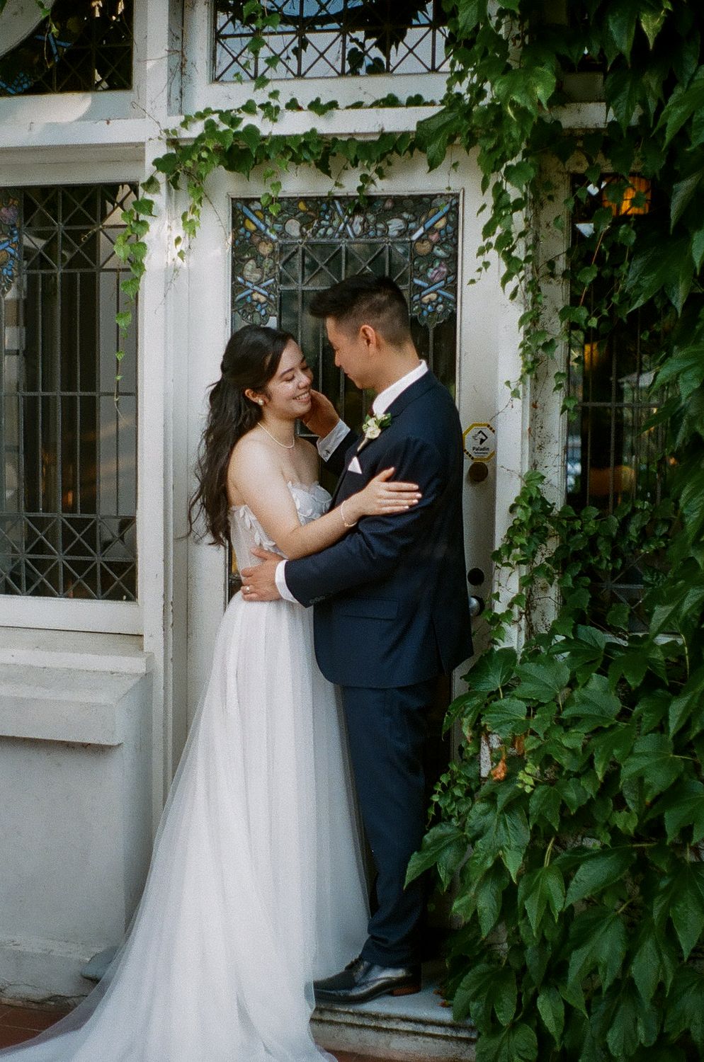Romantic wedding portrait in front of an ivy-covered building with ornate windows.