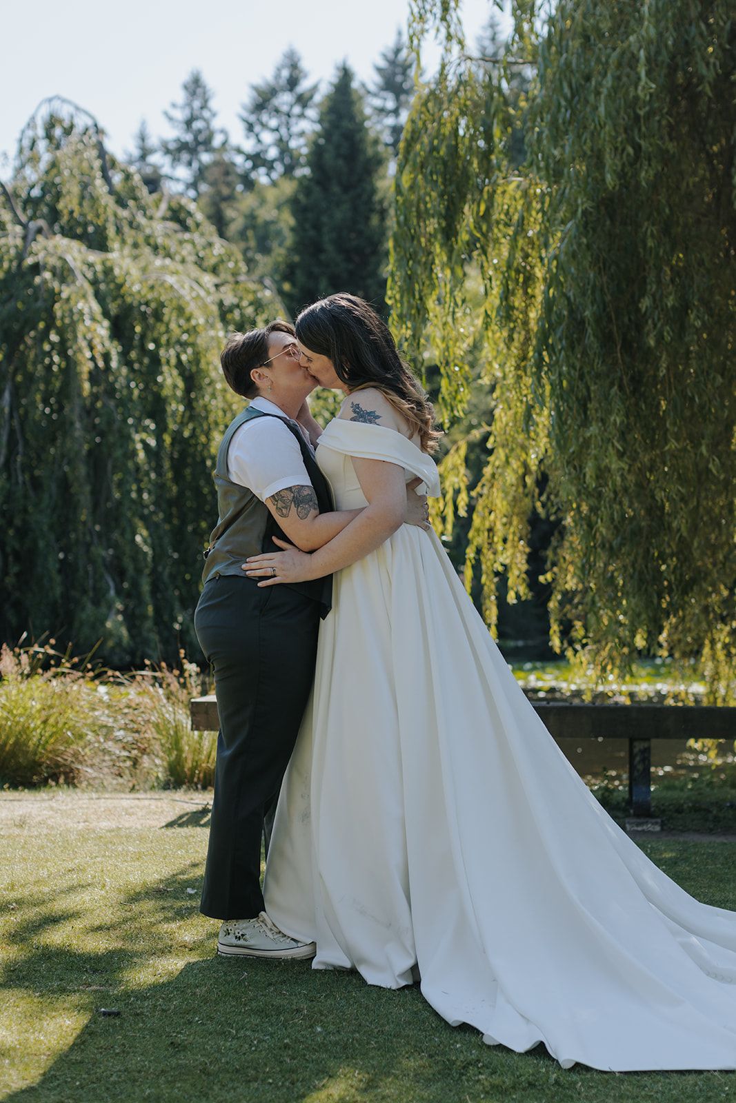 Couple embraces on manicured lawn with cascading willow trees in background.