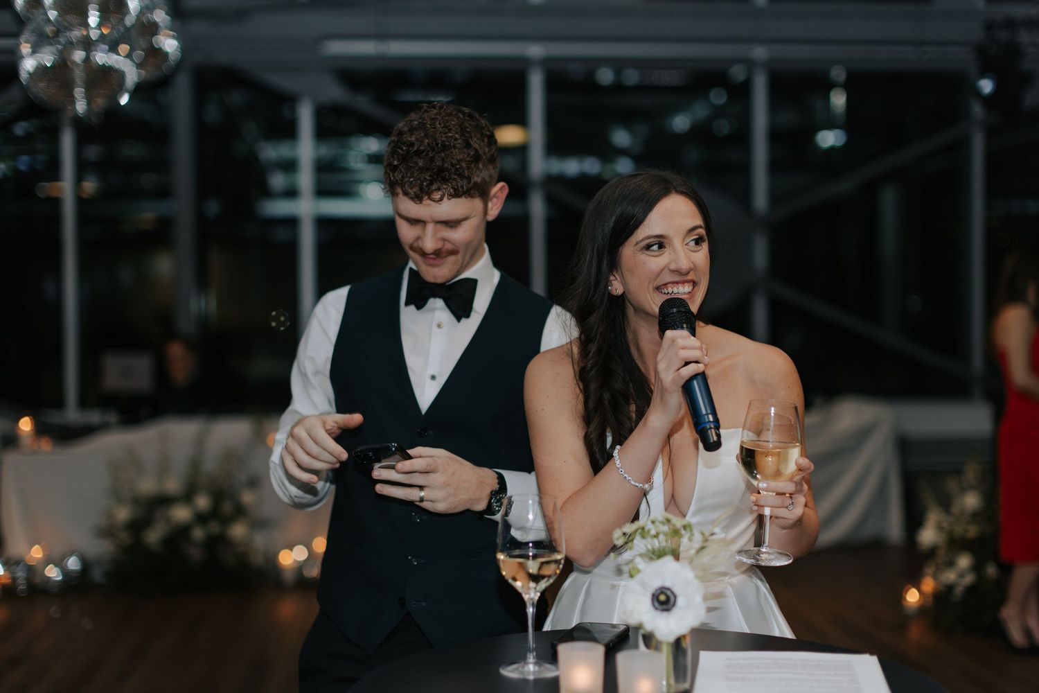 Wedding speeches being given during evening reception with candlelit backdrop.