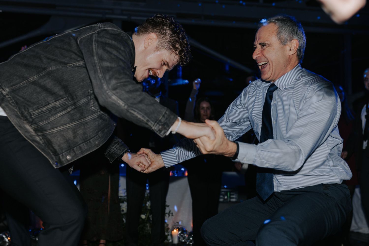 Wedding guests dancing in dimly lit reception venue with blue lighting effects.