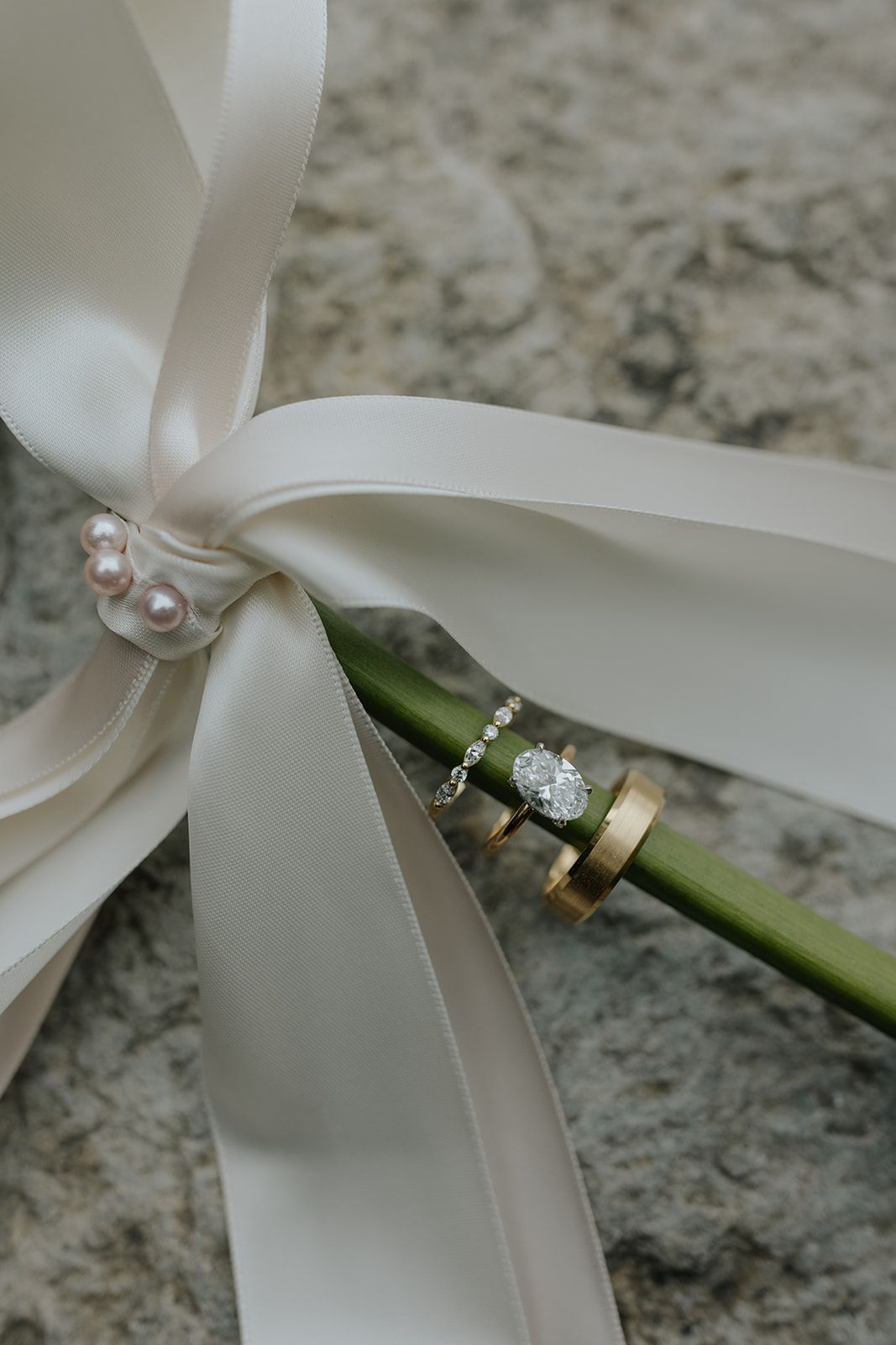Wedding rings and white ribbon arranged artistically on a marble surface.