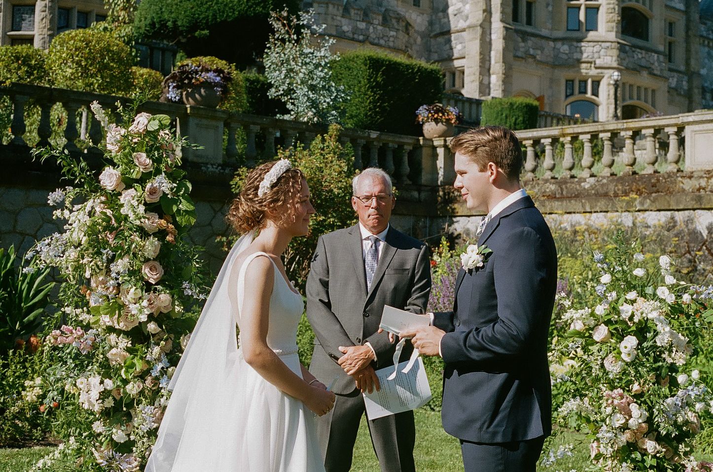 Wedding ceremony taking place in garden of historic stone building.
