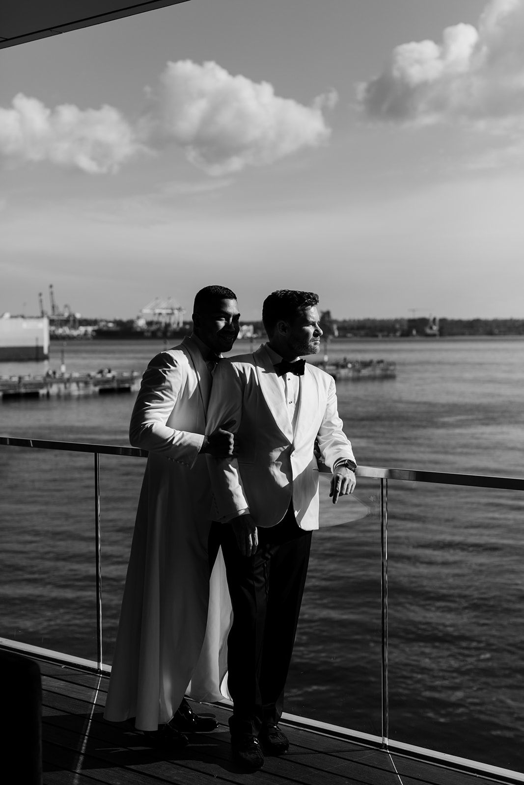 Black and white silhouette of couple looking out over water from a deck railing.