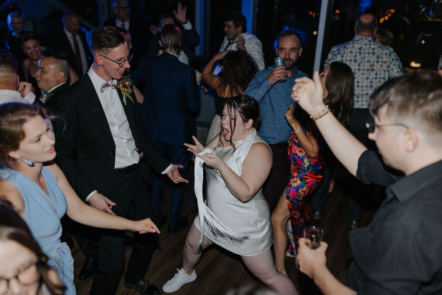 Wedding party dances and celebrates in a dimly lit reception venue.