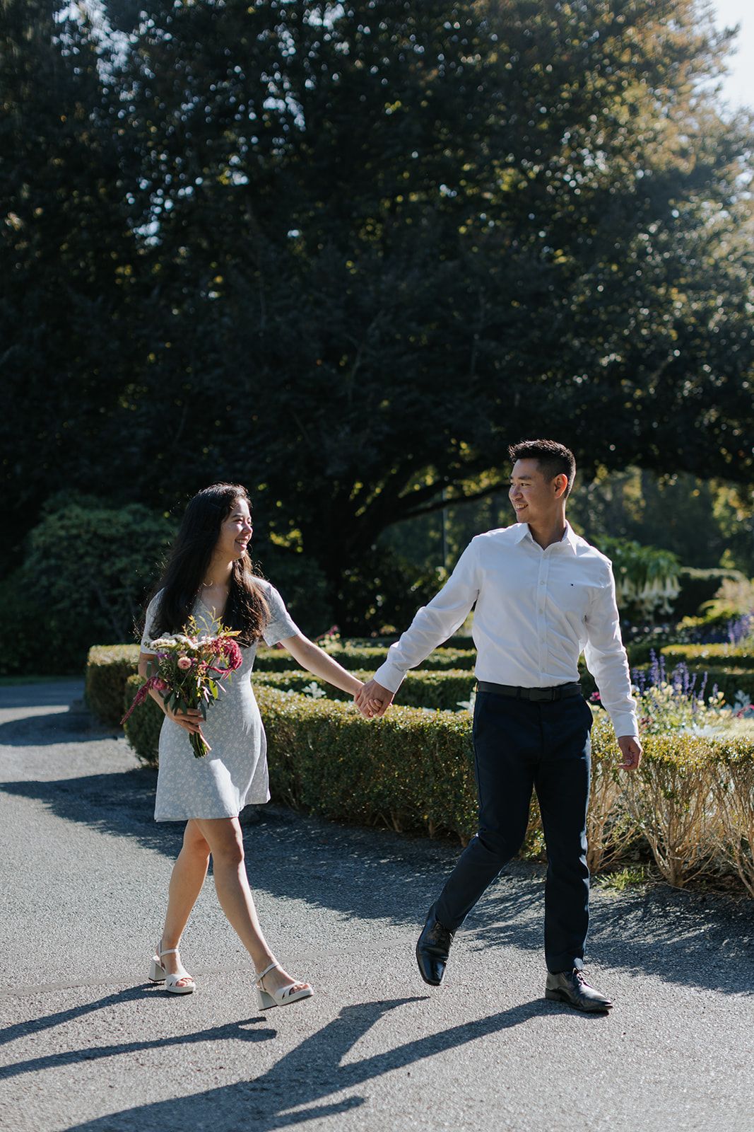 A couple dances playfully on a sunny pathway surrounded by greenery.