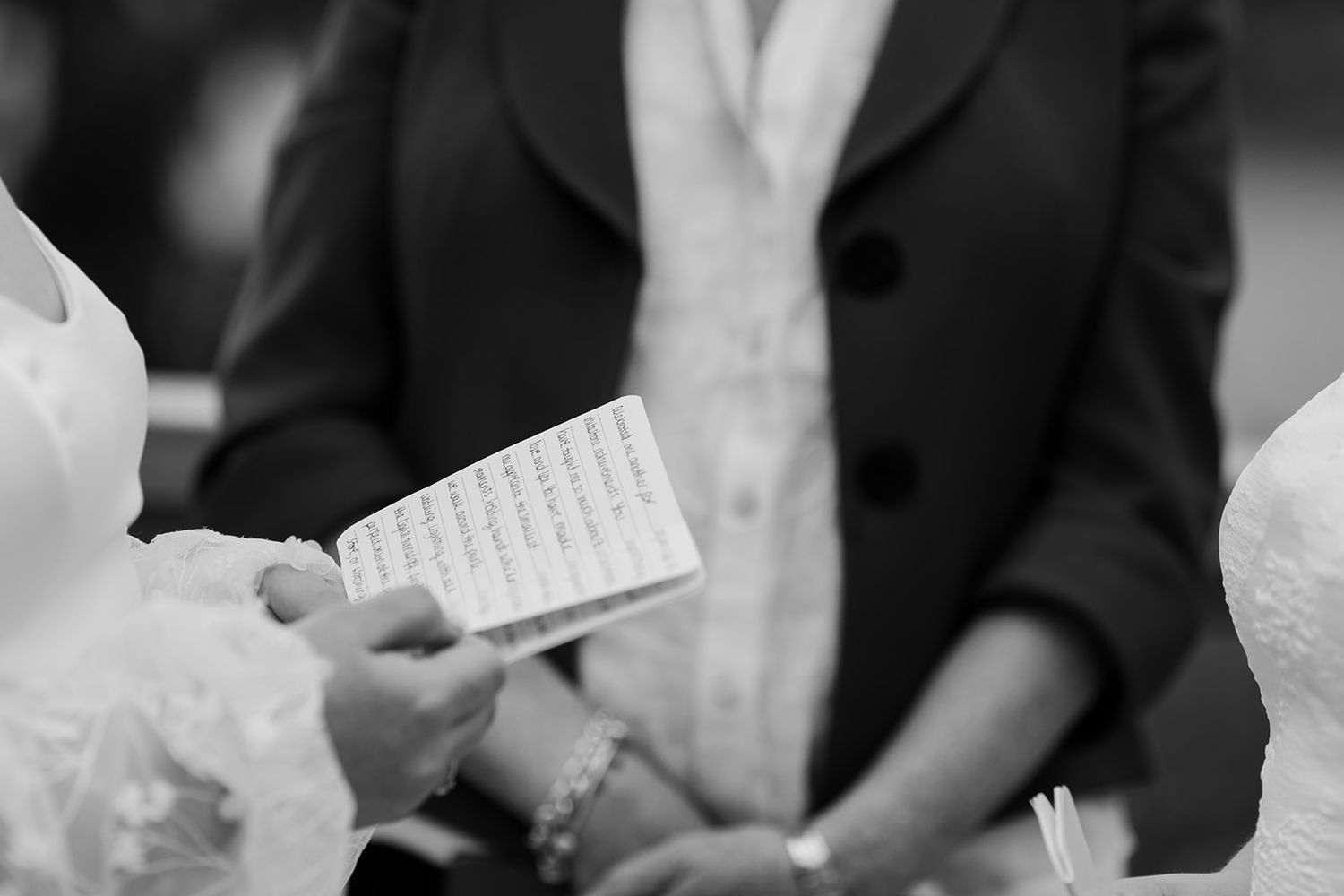 Guests at a wedding ceremony reading from paper programs while seated in formal attire.