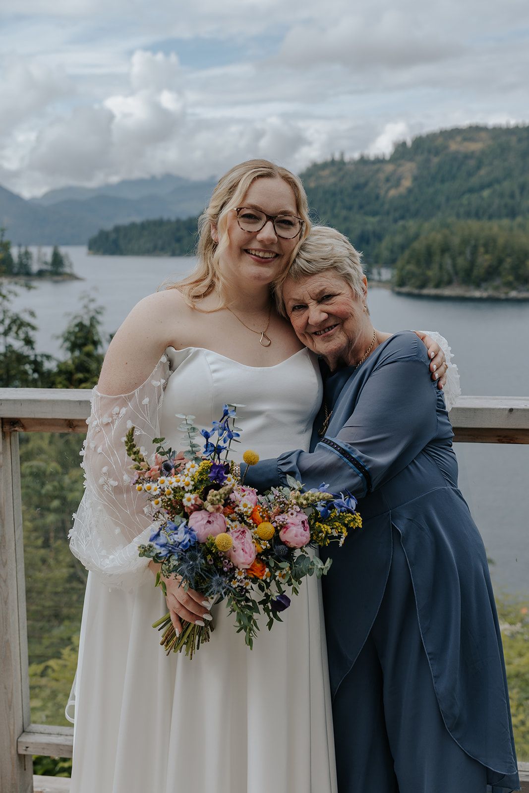 Wedding party members share joyful moments on outdoor deck with scenic mountain backdrop.