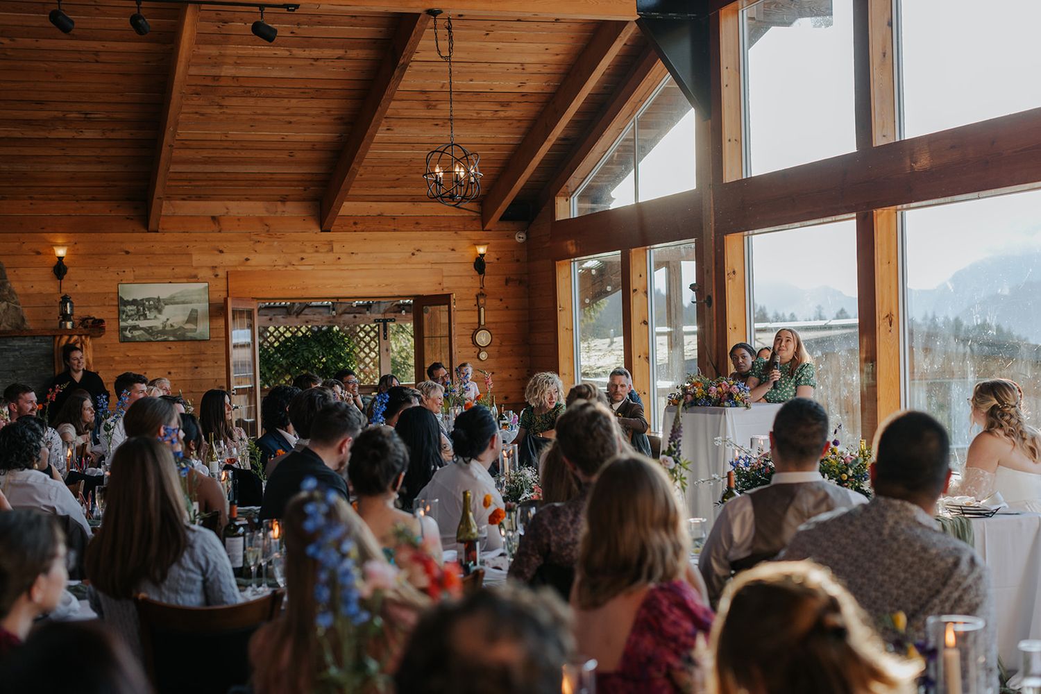 Wide view of wedding reception in rustic lodge with exposed wooden beams.