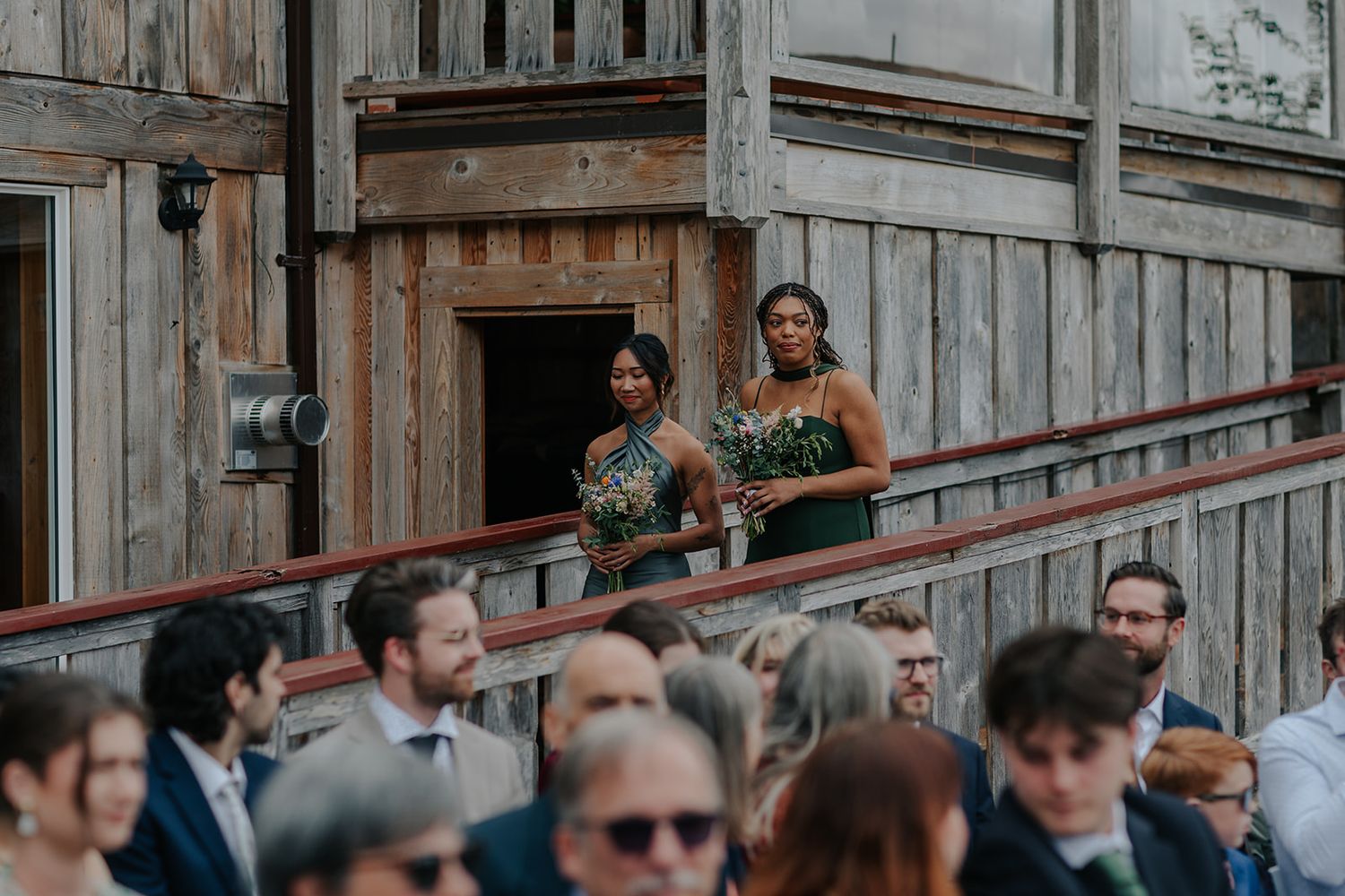 Wedding attendees gather on rustic wooden deck during outdoor ceremony.