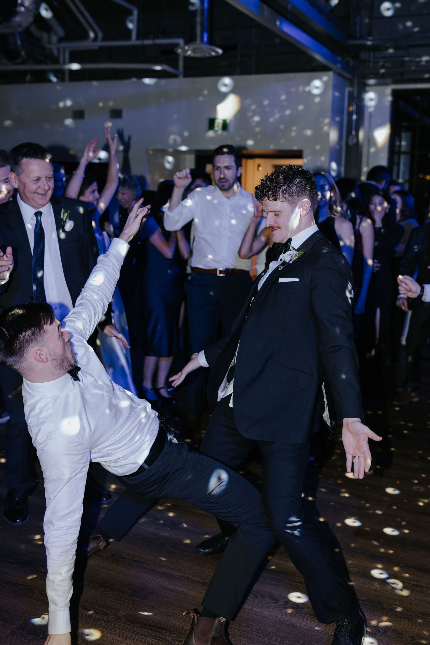 Wedding guests dancing energetically under blue lighting and falling confetti.