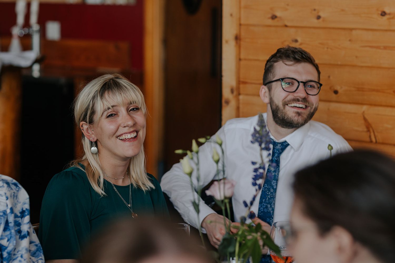 Guests share joyful laughter during wedding reception at rustic venue.