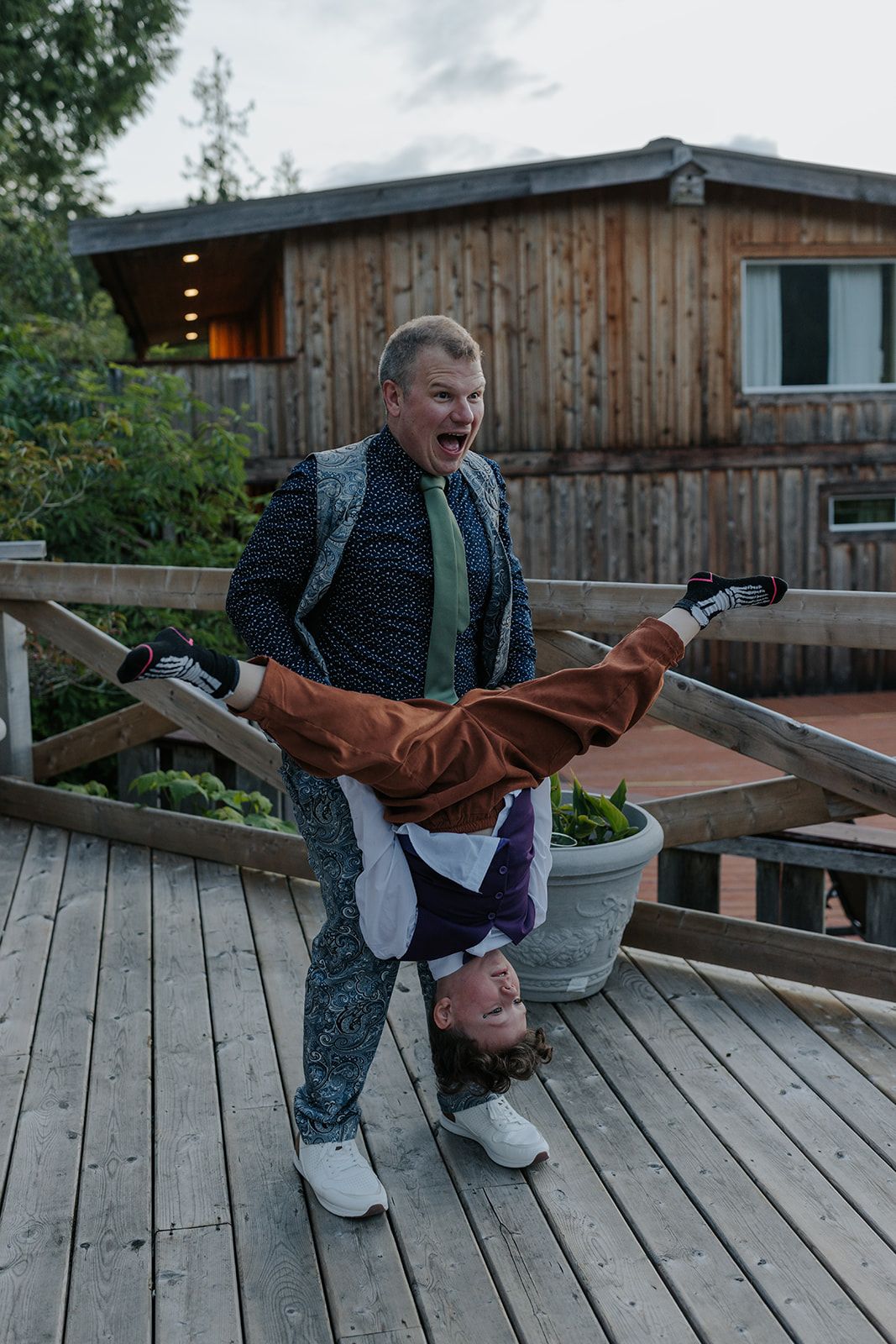 Playful dance move on wooden deck with rustic cabin backdrop during wedding celebration.