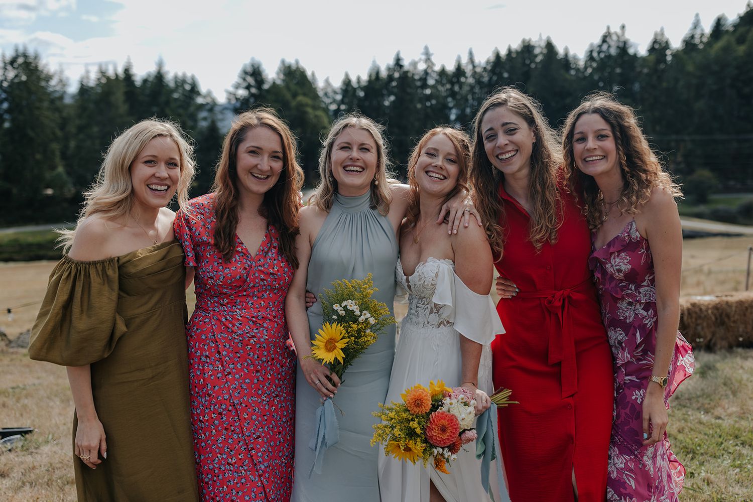 Group of women in colorful dresses celebrating at an outdoor wedding with sunflowers.