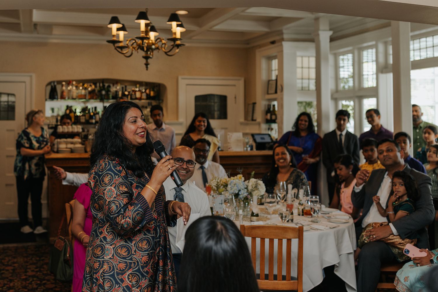 Guests mingle in an elegant reception hall with chandeliers and traditional decor.