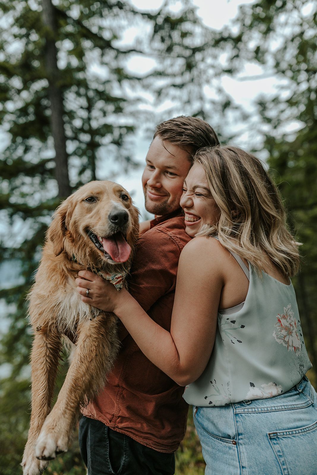 A happy couple embraces while their golden retriever joins in for a joyful outdoor portrait.