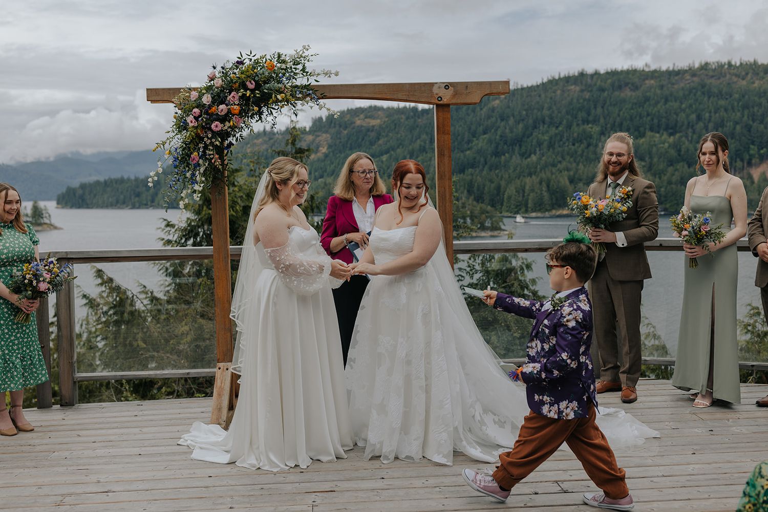 Wedding ceremony setup with wooden arch decorated with flowers overlooking mountain landscape.
