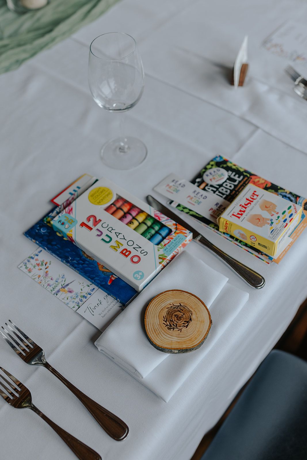 Wedding place setting with wine glass, cutlery, and colorful books on a white tablecloth.