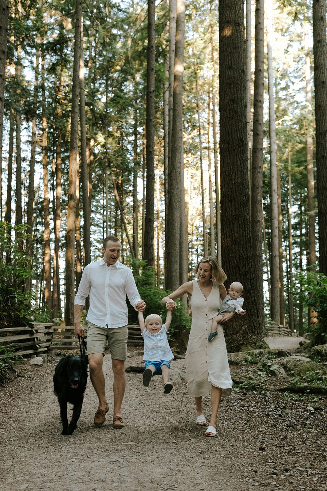 Family walking and playing together on forest trail among tall trees.