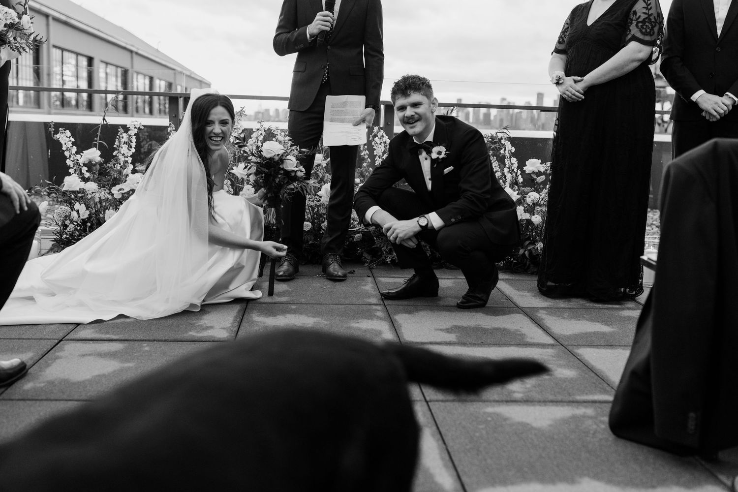 Wedding ceremony guests seated outdoors under cloudy sky at urban venue.