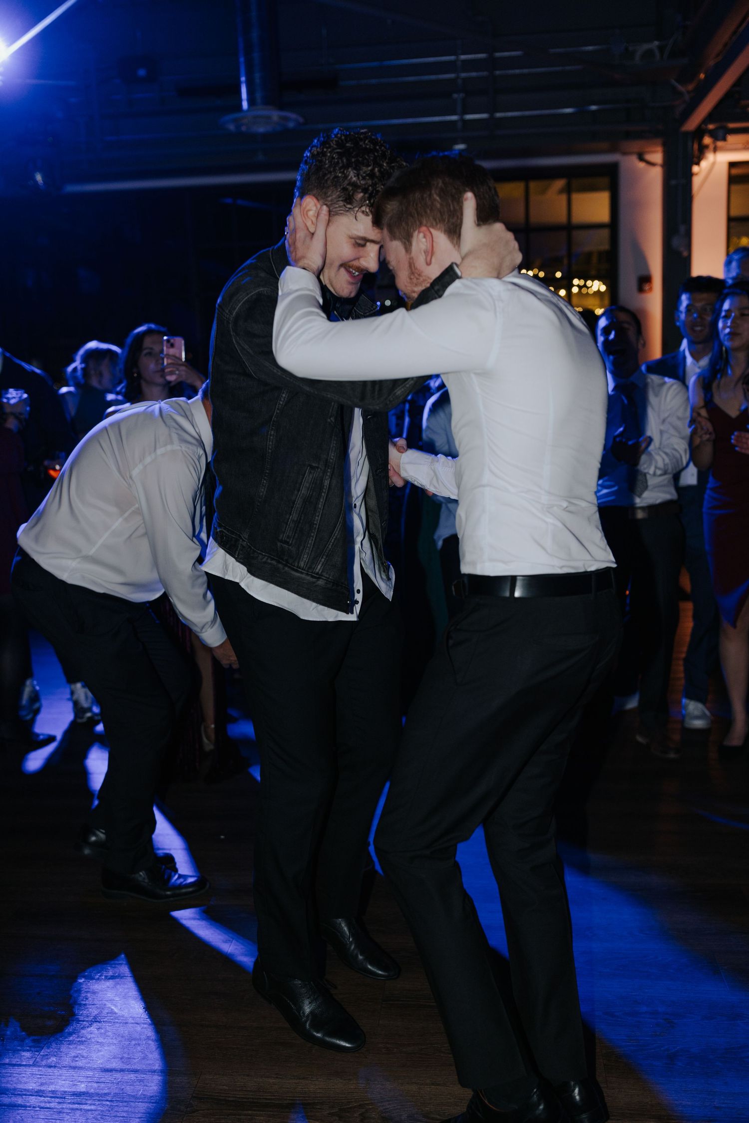 Two guests embrace while dancing at a wedding reception under blue lighting.