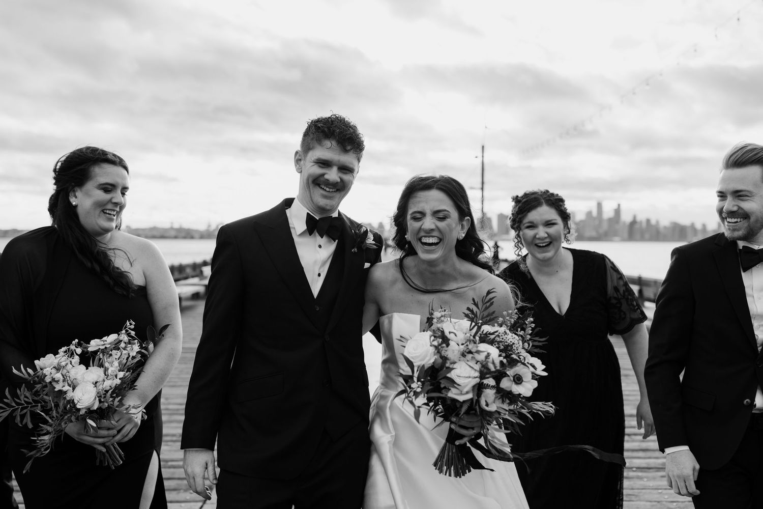 Black and white photos of a wedding party laughing together on a pier.