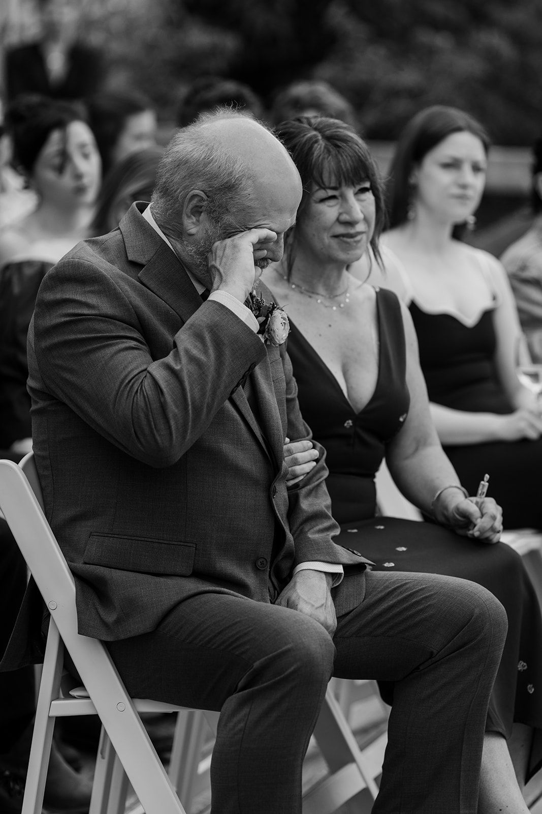 Wedding guests seated in formal attire during an emotional outdoor ceremony moment.