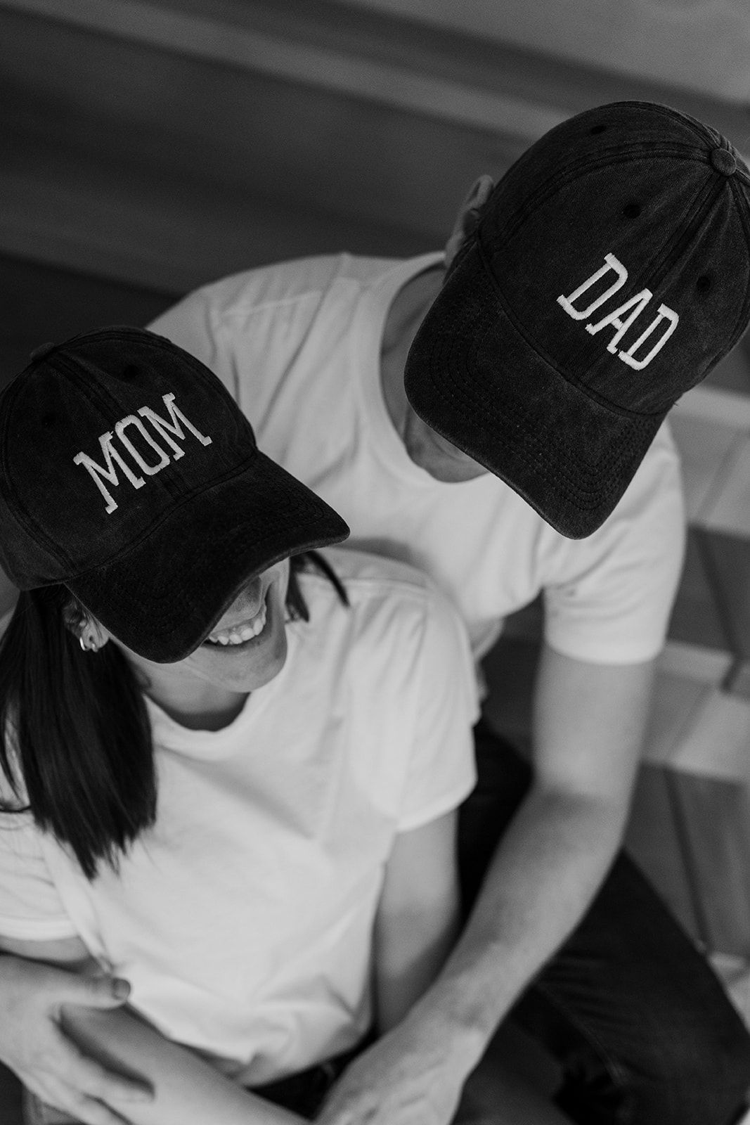 Black and white photo of two people wearing baseball caps with 'Mom' and 'Dad' text.