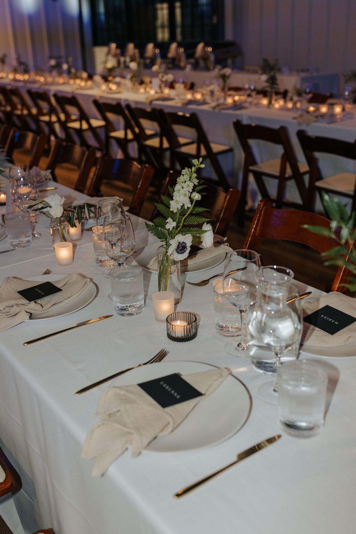 An elegant wedding reception table setting with candles, white linens, and delicate floral centerpieces.