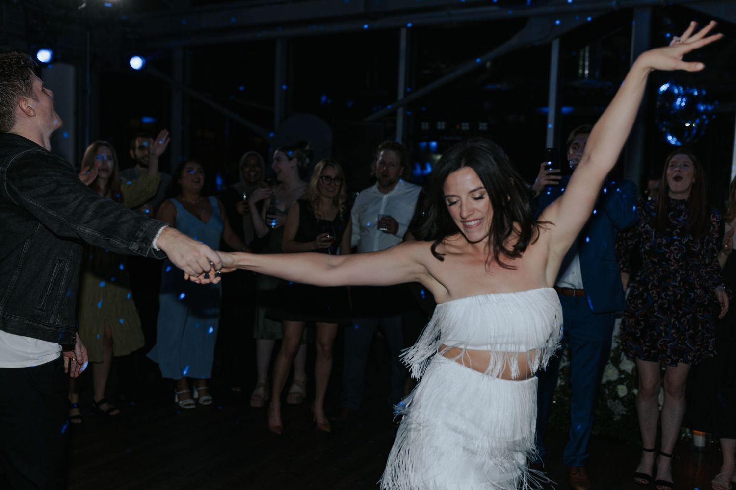 Dancers celebrating at a dimly lit nightclub with raised arms and energetic movements on the dance floor.