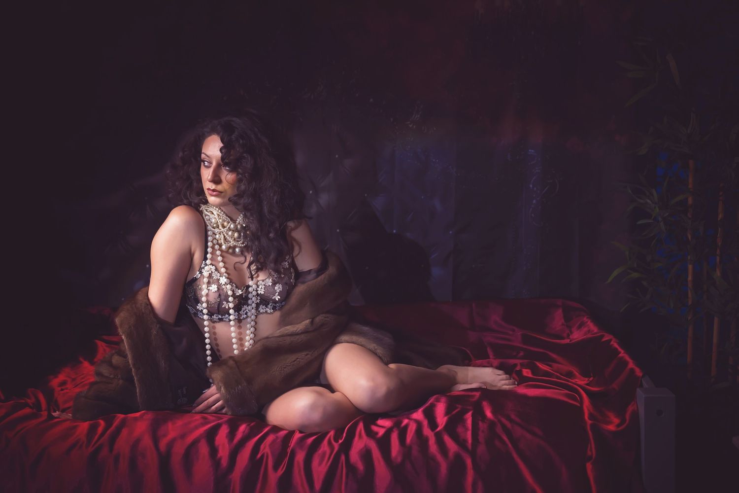 Boudoir photo on dark red bedding with moody lighting.