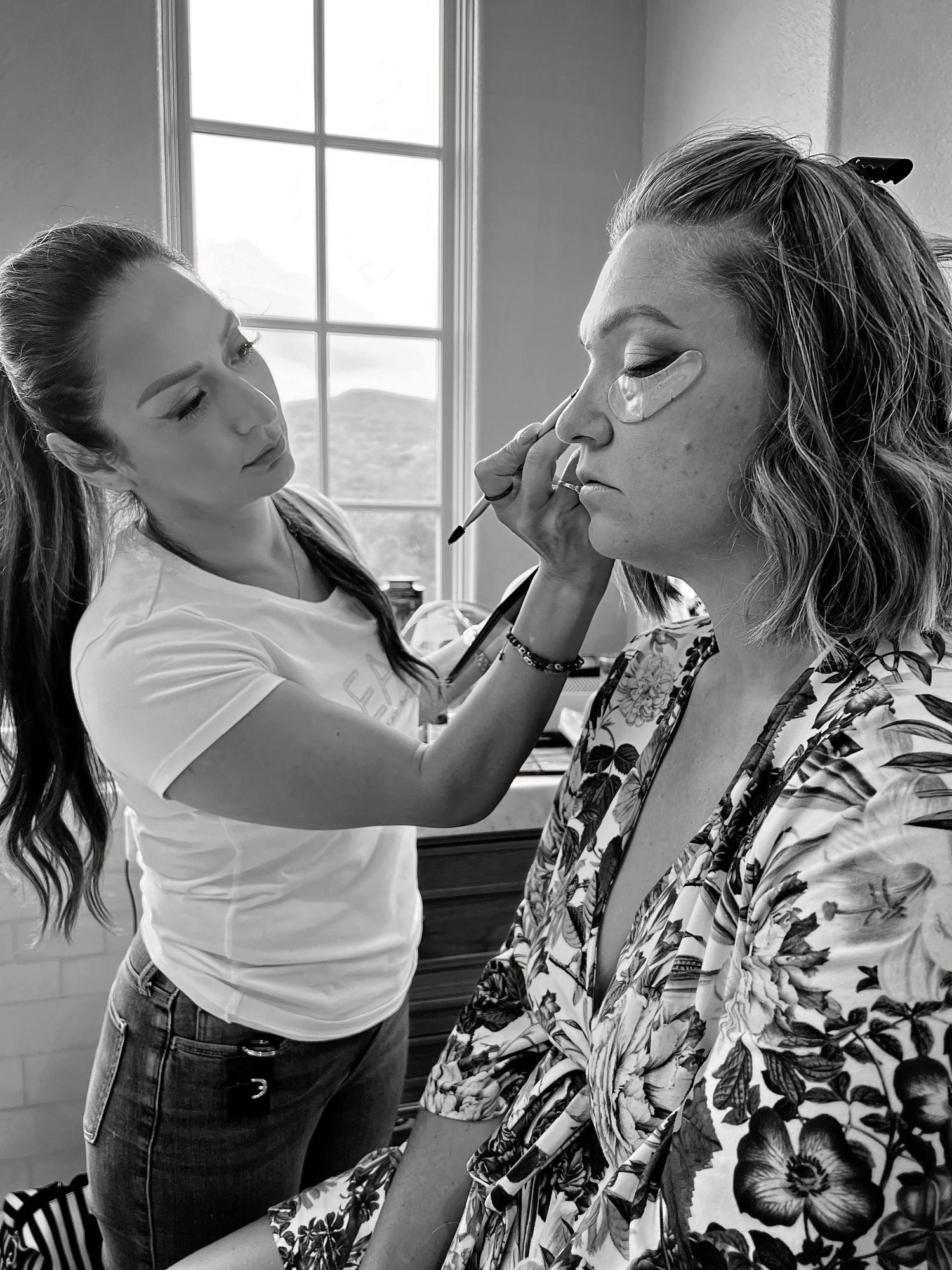 black and white photo of makeup artist placing eye make up on a client