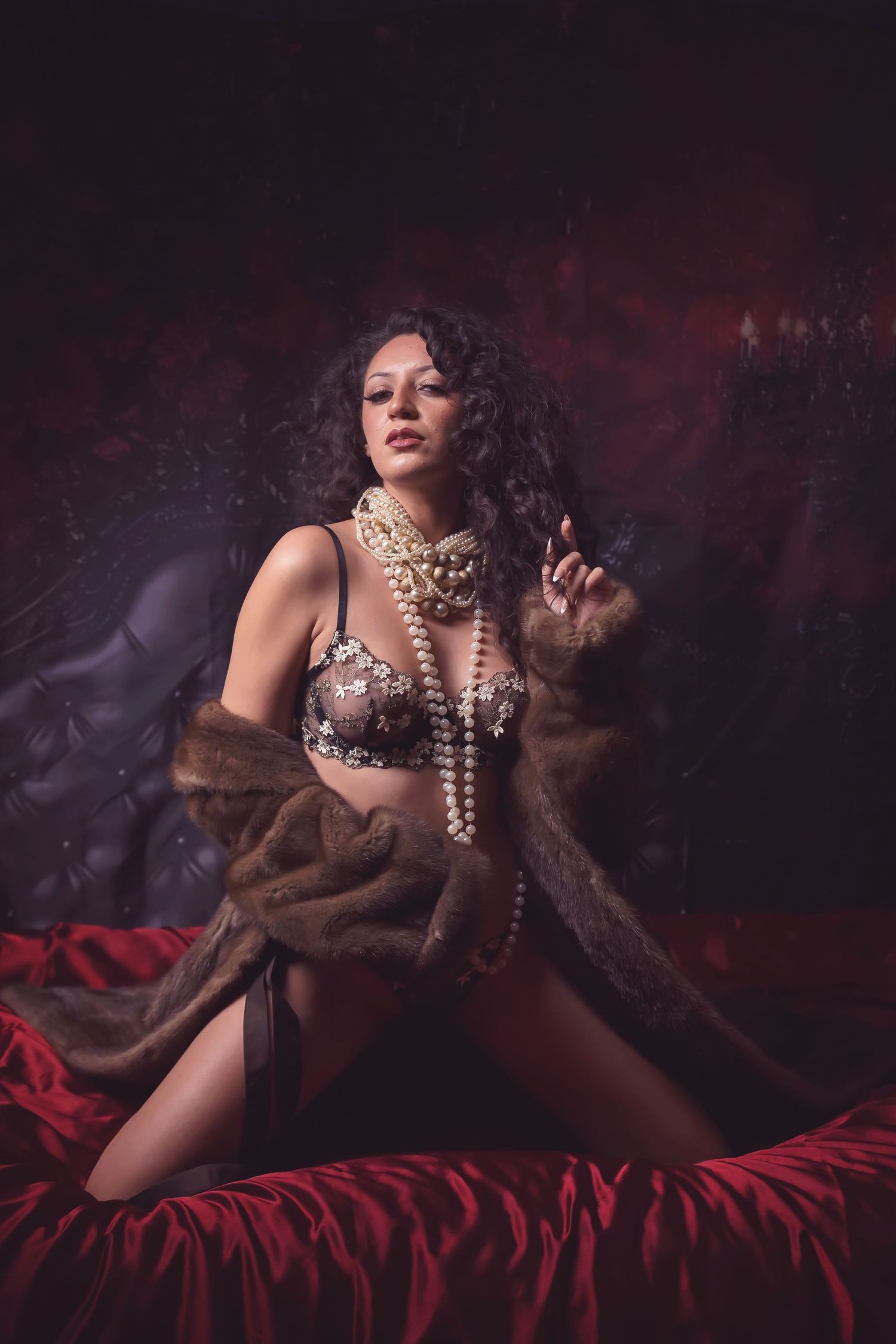 Glamour portrait with pearl necklaces and fur wrap on red bedding.