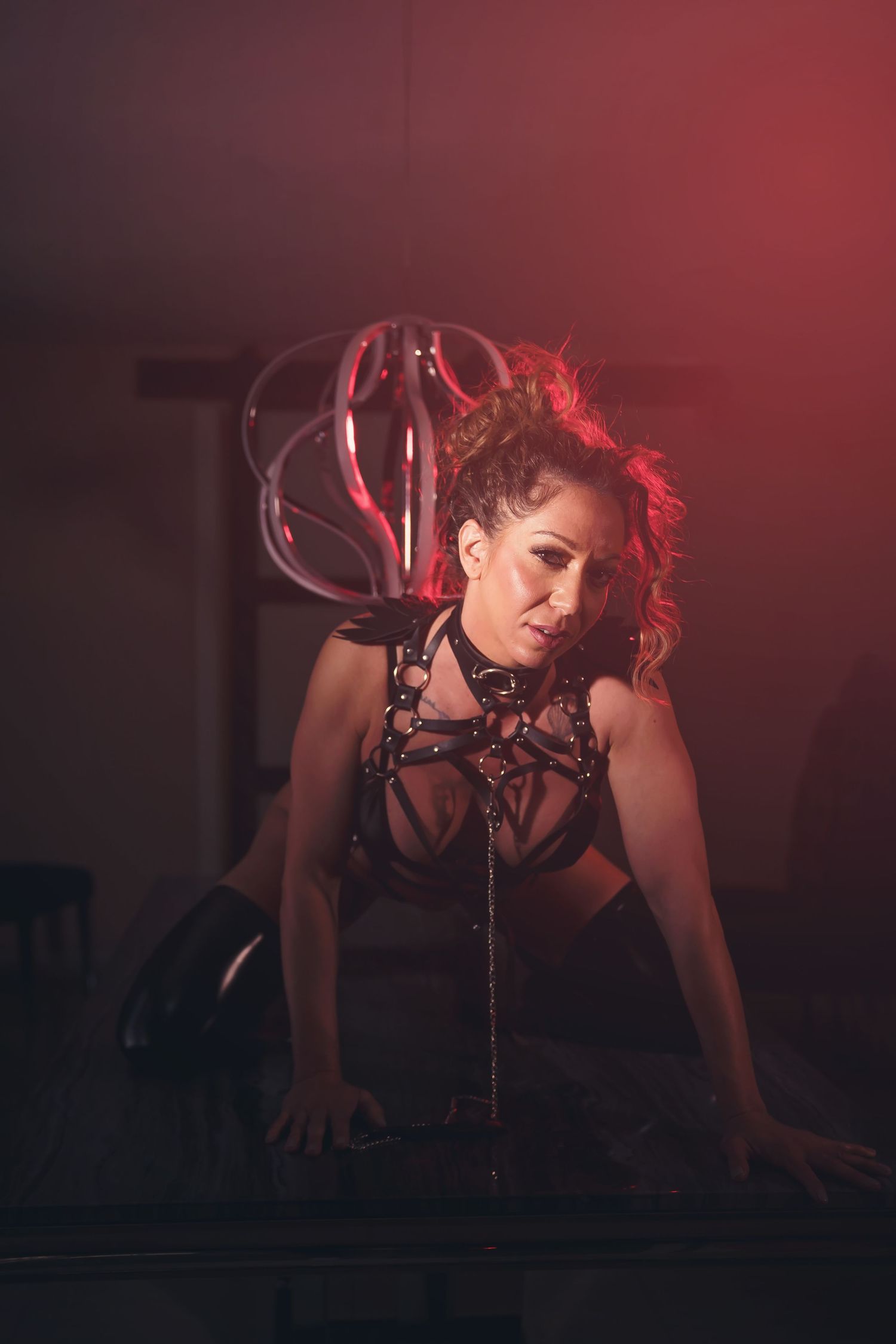Dramatic red-lit studio portrait with harness outfit and glass prop.