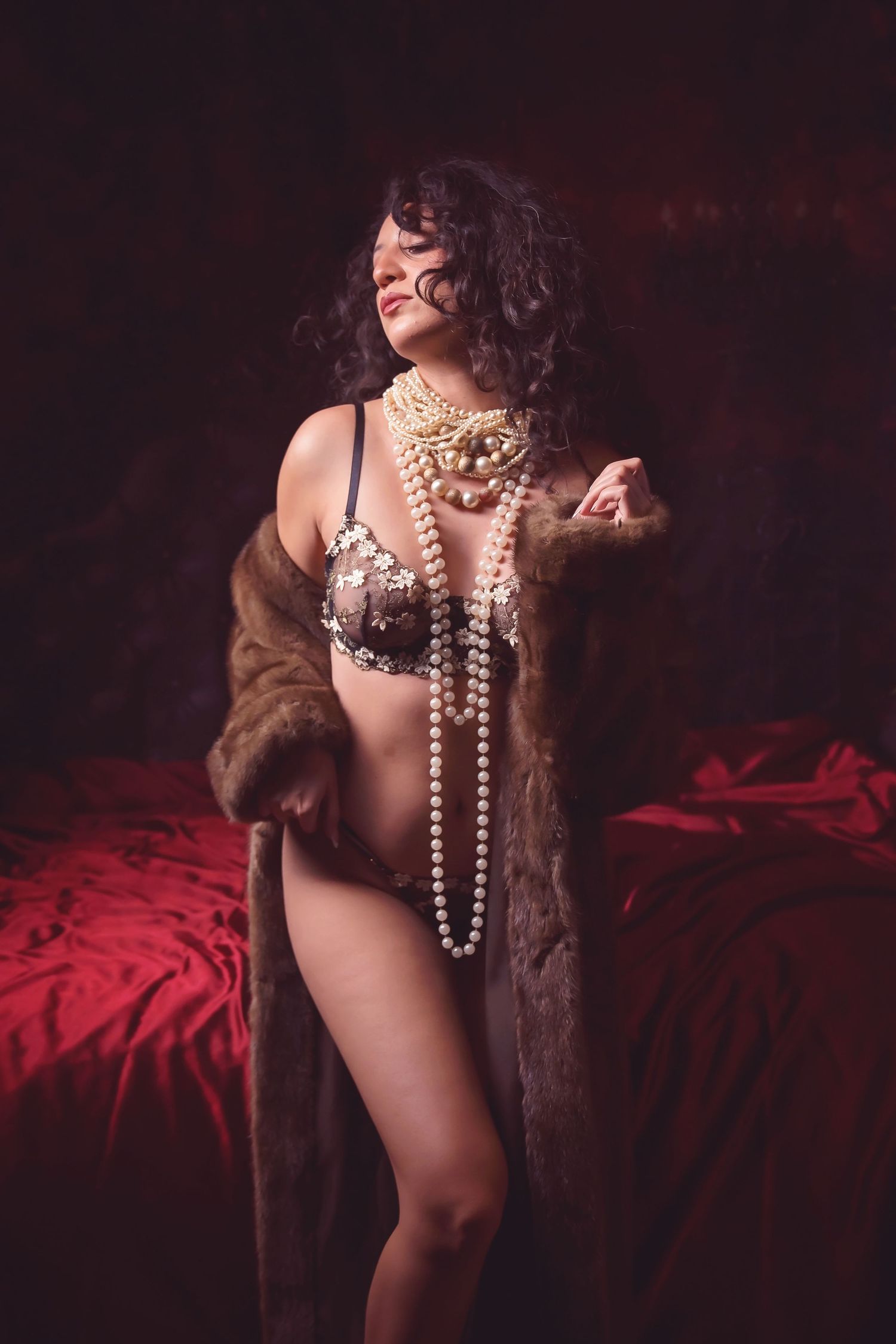Elegant portrait with pearl accessories and fur wrap against dark background.