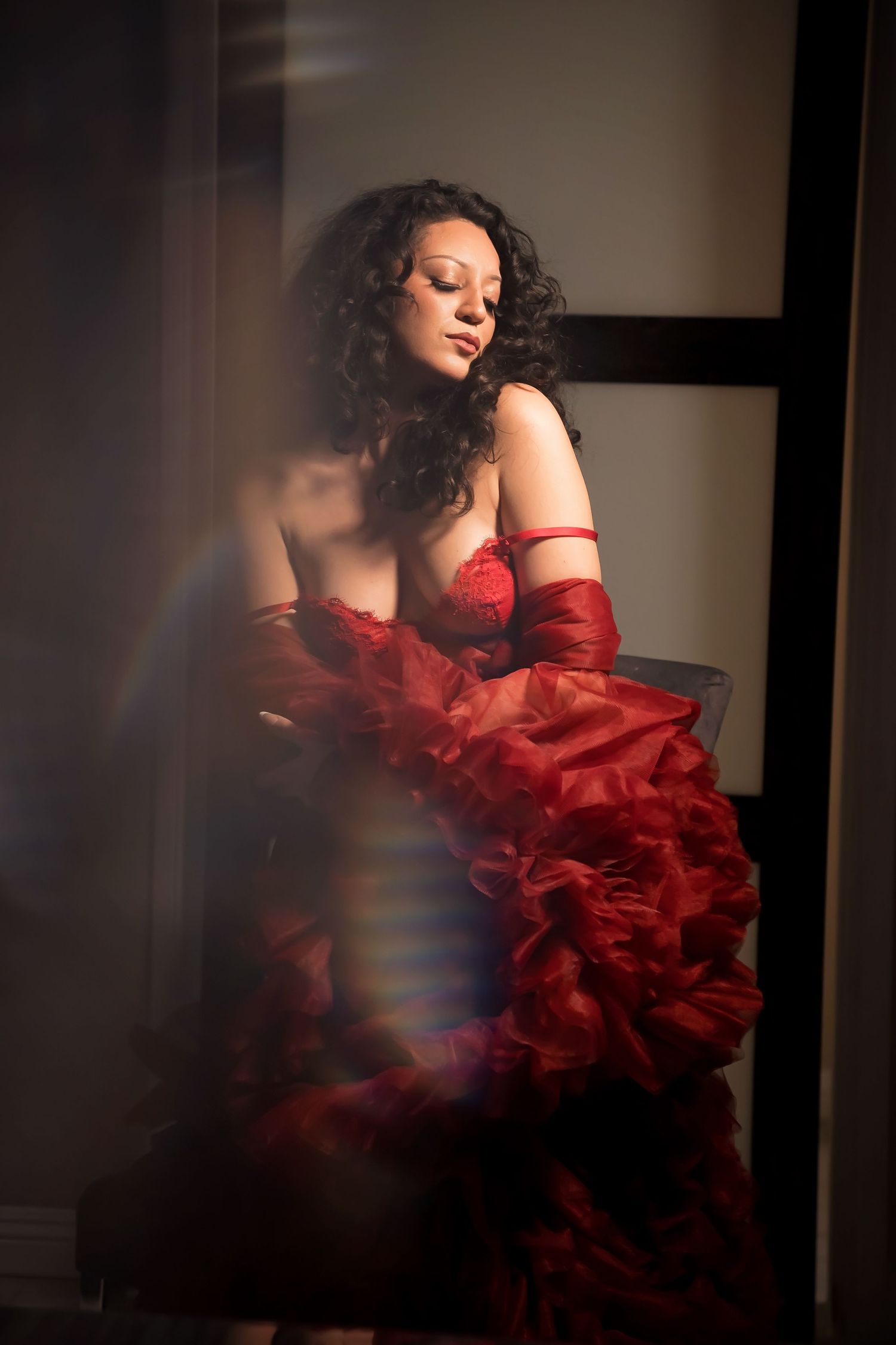 Artistic portrait with model in flowing red dress and matching gloves in shadowy setting.