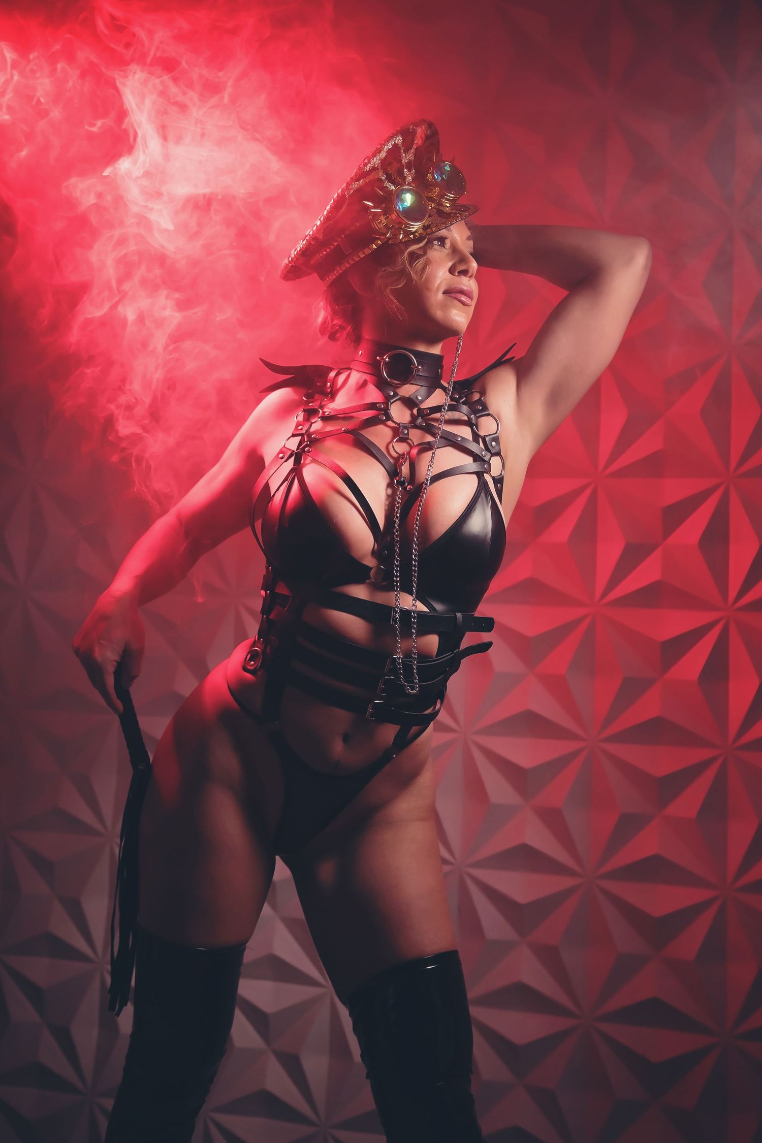 Dramatic boudoir photo with red smoke effects and geometric background lit in crimson lighting.