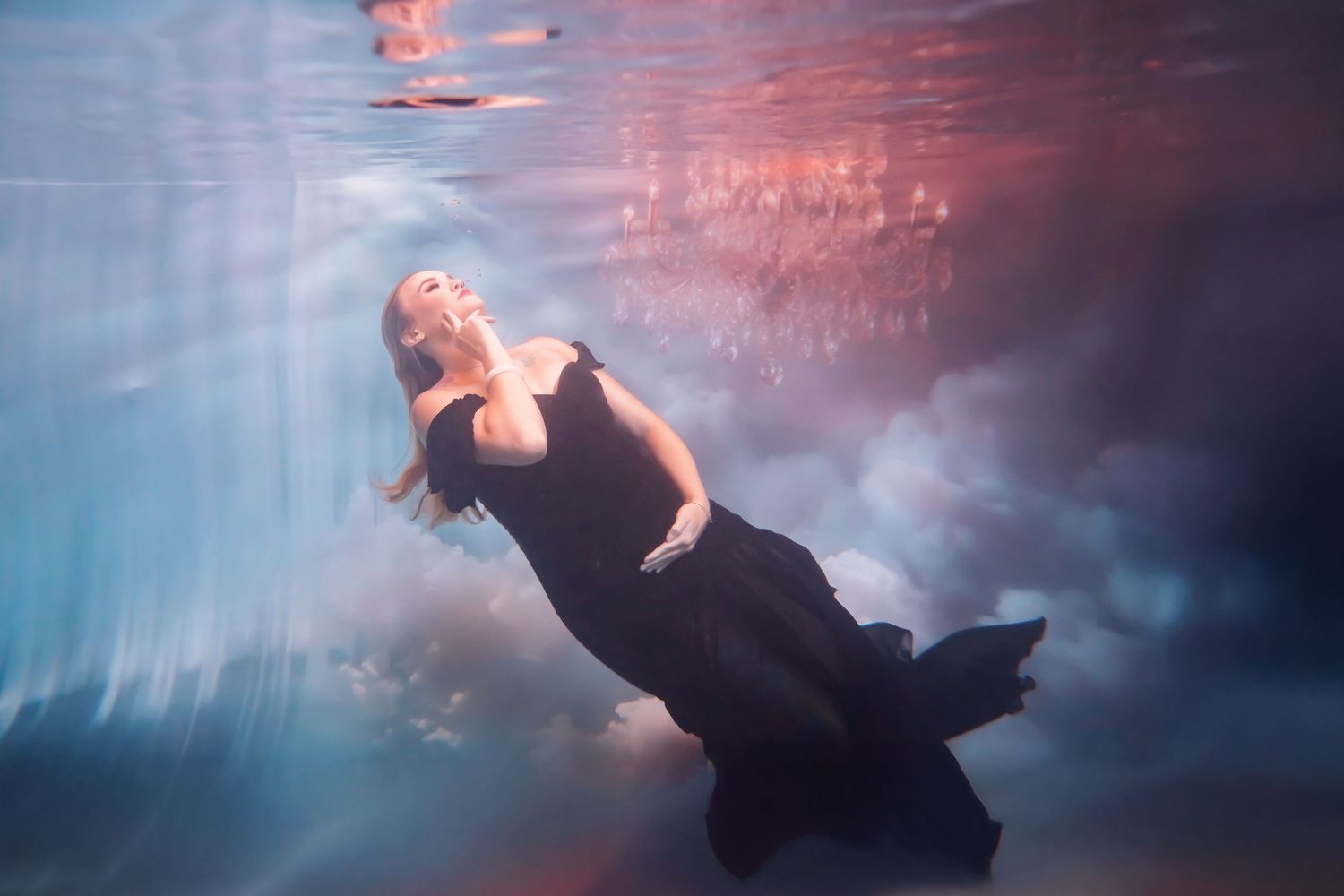 pregnant woman floating underwater with flowing gown reflections create an ethereal underwater scene with swirling shades of pink and blue.