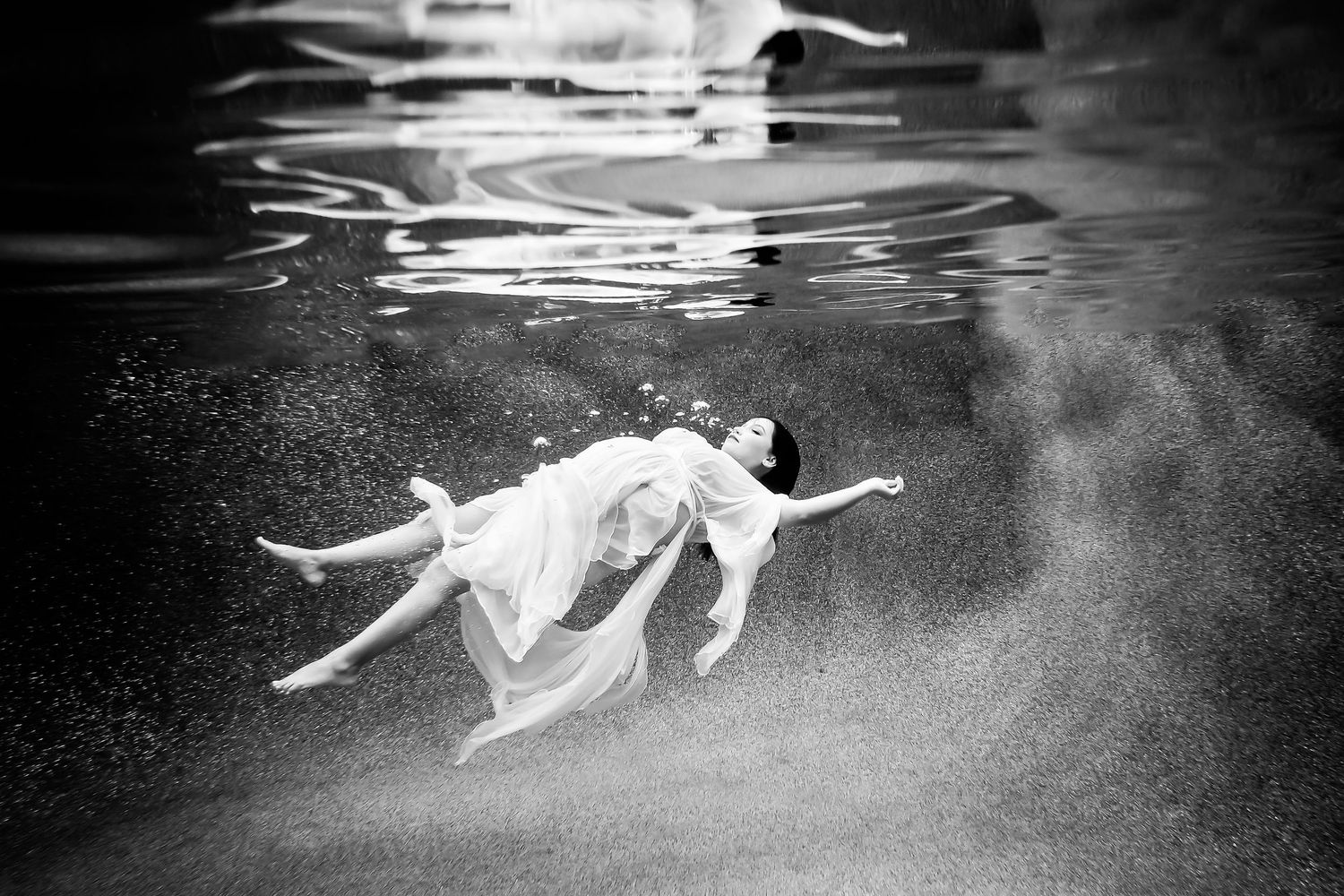 Black and white maternity underwater series showing graceful fabric movements creating artistic light patterns.