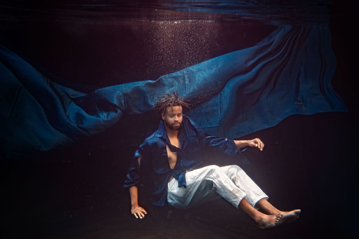 Ethereal underwater-style photography with flowing blue fabric creating dramatic movement.