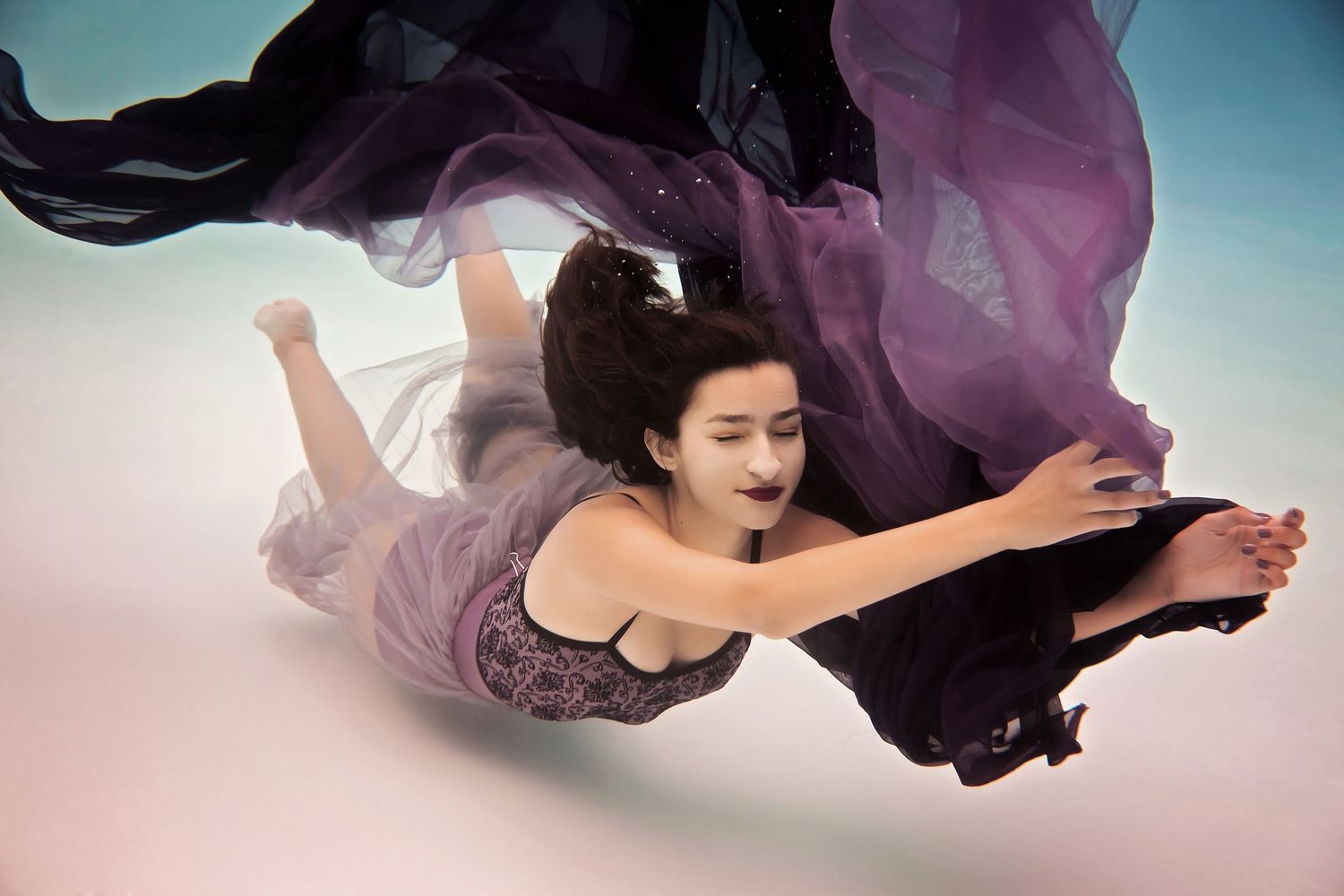 Dynamic motion photography underwater with billowing purple fabric against a gradient sky background.