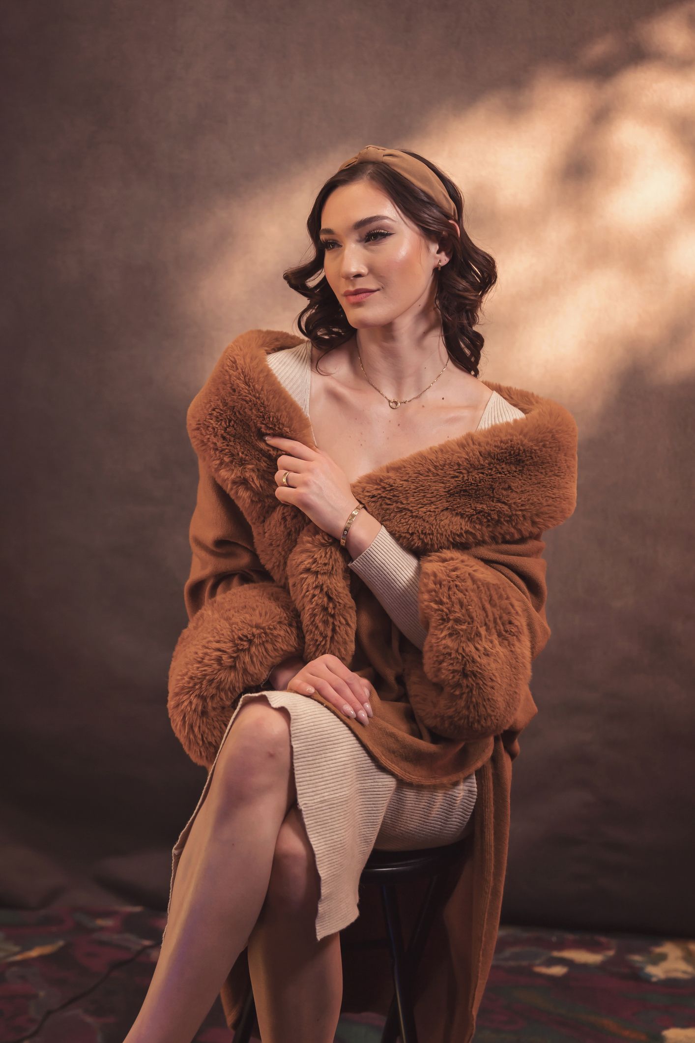 Glamour portrait session featuring warm brown fur coat and elegant beige dress against moody brown backdrop.