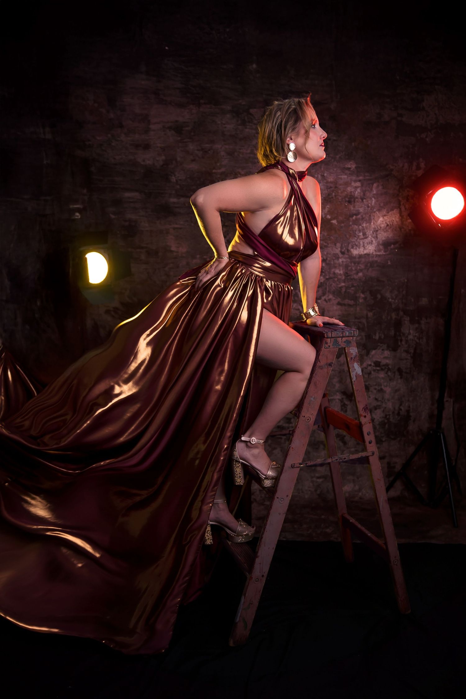 Dramatic lighting and flowing dress create dynamic poses against brick wall.