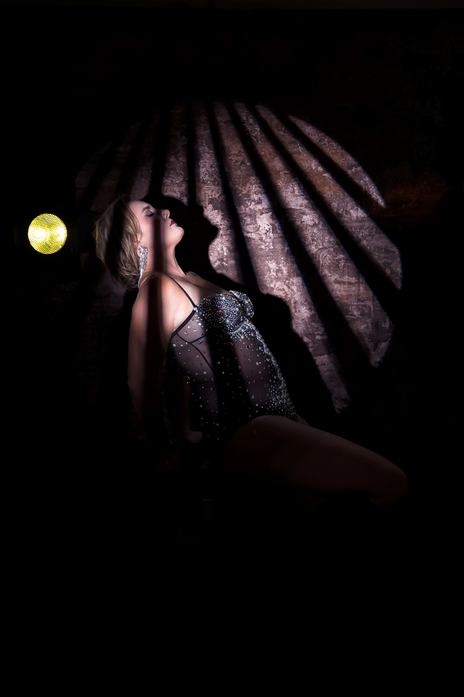 Diagonal shadows from blinds cast dramatic patterns on a wall highlighting a female creating a moody atmospheric effect.