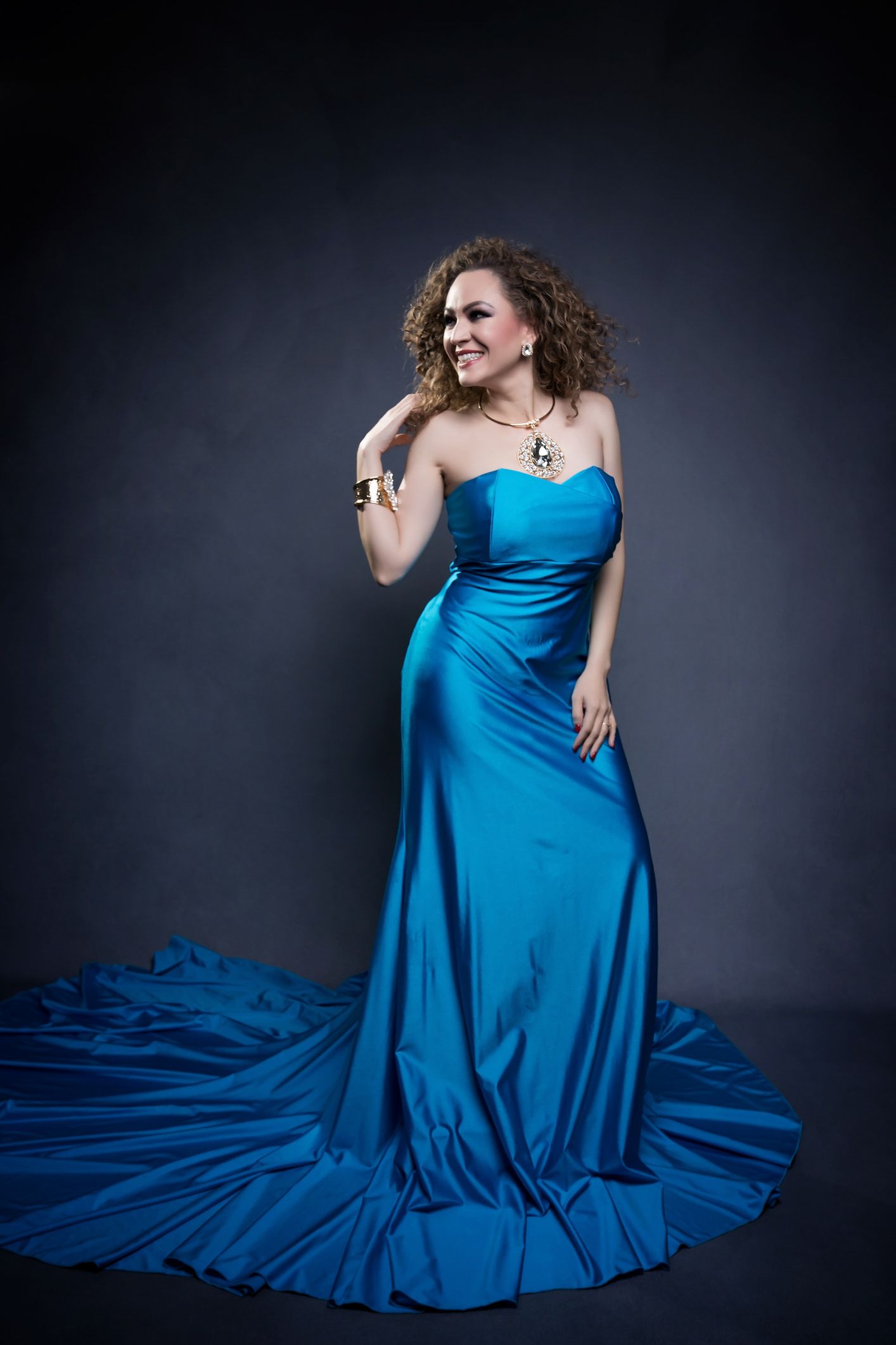 Vibrant royal blue satin gown flows dramatically across the floor in studio lighting.