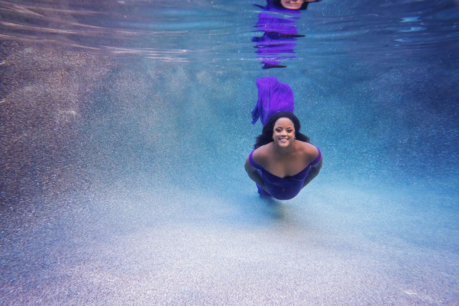 Underwater maternity portrait with purple lighting showing submerged figure in pool.