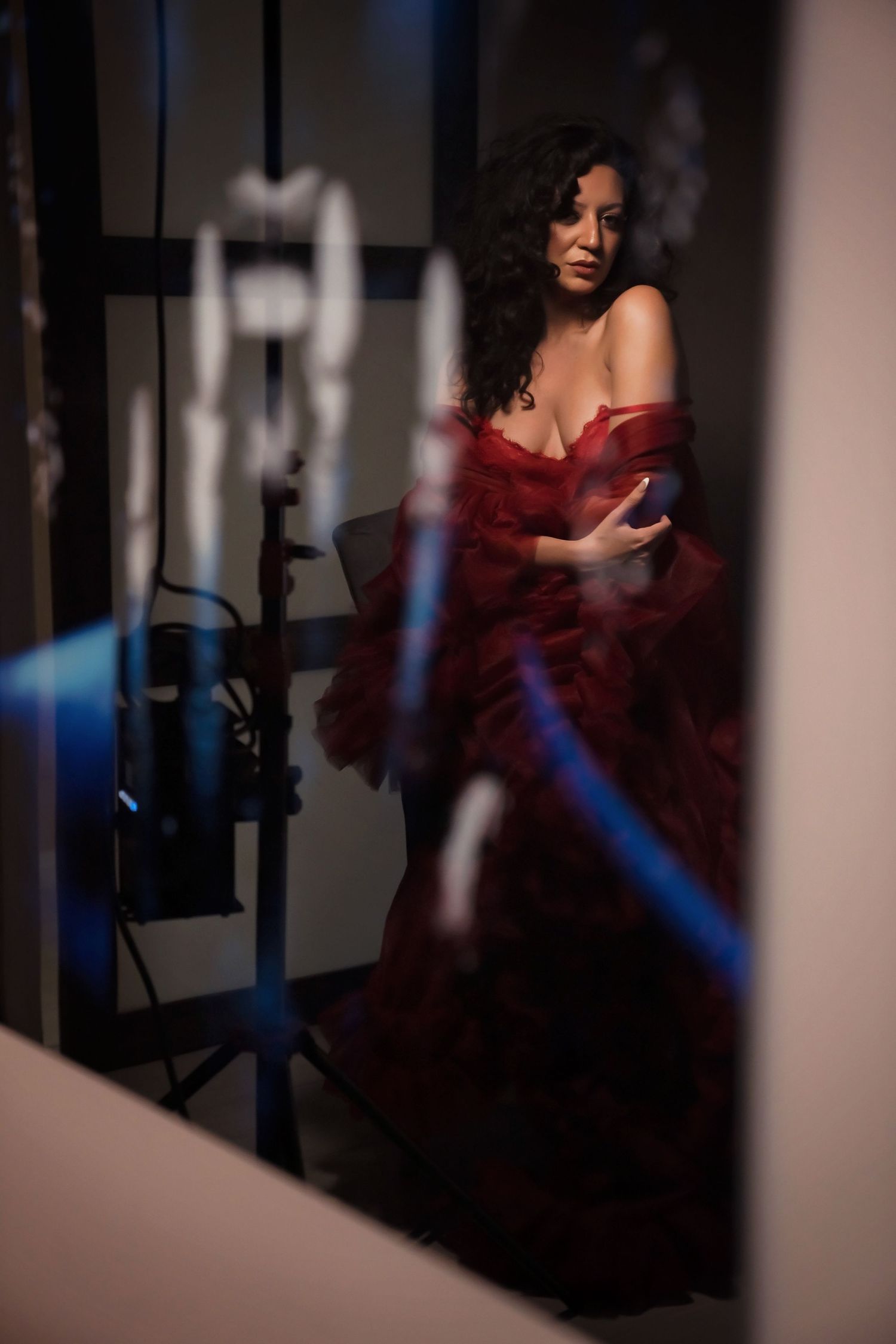 Behind-the-scenes photo showing model in red dress with lighting equipment visible.